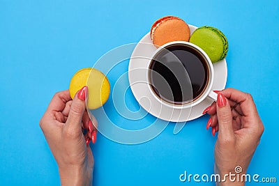 Hands of woman holding a colorful cookies and a cup of coffee over turquoise flatlay Stock Photo