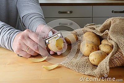 Hands of a woman are peeling raw potatoes with an old peeler on a wooden kitchen table Stock Photo