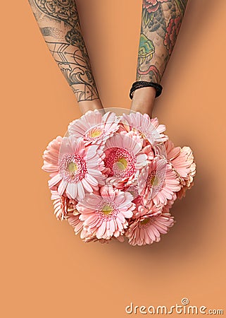 Hands of a woman with a tattoo hold a beautiful bouquet with pink gerberas on an orange background Editorial Stock Photo
