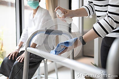 Hands of woman using spraying alcohol antiseptic,daughter is cleaning walking aids,walker for her elderly mother,during Stock Photo