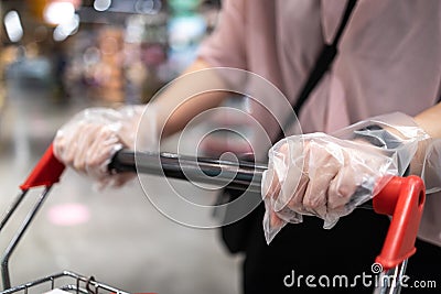 Hands of woman wearing plastic gloves pushing a shopping cart,prevent spread infection of COVID-19,Coronavirus,plastic gloves Stock Photo