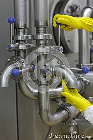 Hands in yellow gloves on tap and lever of technological system Stock Photo