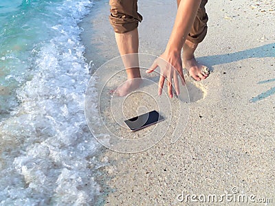 Hands of young Asian man dropping mobile smart phone on tropical sandy beach. Accident and insurance electronic equipment concept Stock Photo