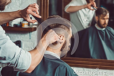 The hands of young barber making haircut to attractive man in barbershop Stock Photo