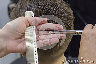 The hands of young barber making haircut to attractive man in barbershop. mens hair cutting scissors Stock Photo