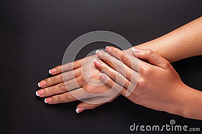 The hands of a young girl are covered with a highlight top. French manicure. Hands on a black background Stock Photo