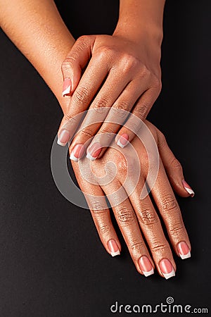 The hands of a young girl are covered with a highlight top. French manicure. Hands on a black background Stock Photo