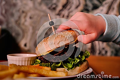 Hands of a young girl holding hamburger. Ready to eat. Concept photo of child obesity, unhealthy eating, unhealthy food Stock Photo