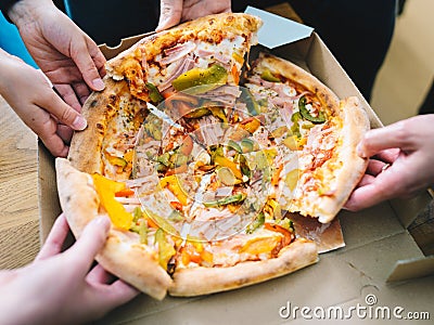 Hands of young people taking pizza slices from delivery cardboard box dining together, friends sharing meal having lunch at home Stock Photo