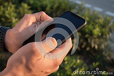 Hands of a young person using his smart phone on the outside. It`s the sunset Stock Photo