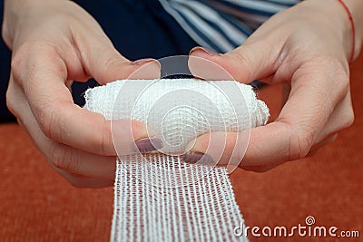 Hands of a young woman unwind a roll of a medical gauze bandage. Frontal close-up view. Selective focus Stock Photo