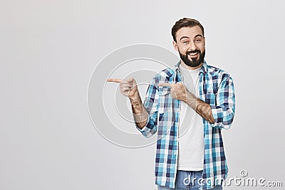 Handsome adult spouse with beard and moustache, smiling and expressing cheer while pointing left with two hands Stock Photo