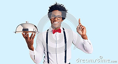 Handsome african american man with afro hair wearing waiter uniform holding silver tray surprised with an idea or question Stock Photo