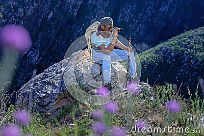 A Young African male hiking in the mountains amongst pink fynbos flowers during spring time in South Africa Stock Photo