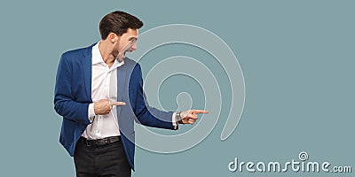 Handsome amazed bearded man in blue suit standing and pointing a Stock Photo