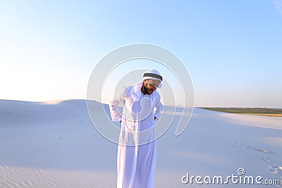 Handsome Arab sheik suffers from discomfort in back, standing in Stock Photo