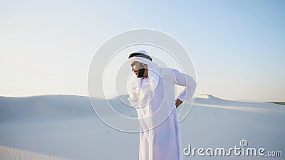 Handsome Arab sheik suffers from discomfort in back, standing in Stock Photo