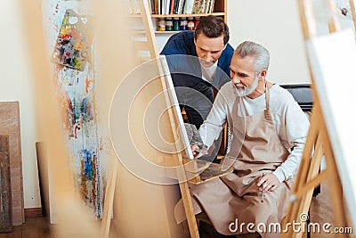 Handsome artist helping elderly man in painting Stock Photo