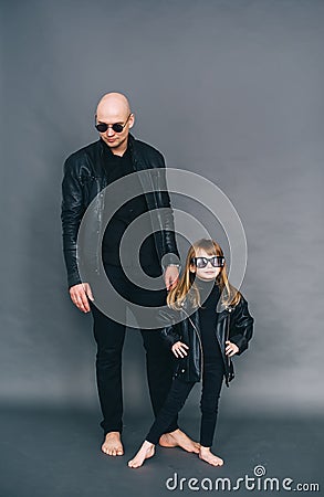 Handsome bald father with his little daughter in black sunglasses and in leather jackets are posing in studio Stock Photo