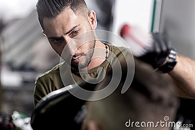 Handsome barber dries hair and makes a styling of dark-haired man at a barbershop Stock Photo