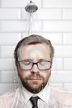 Handsome bearded man in glasses, shirt and tie stands in bathroom under the warm water that comes from the watering can and with Stock Photo
