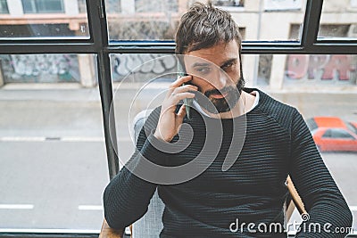 Handsome bearded man using his smartphone for making call at modern home. Blurred background. Horizontal. Stock Photo