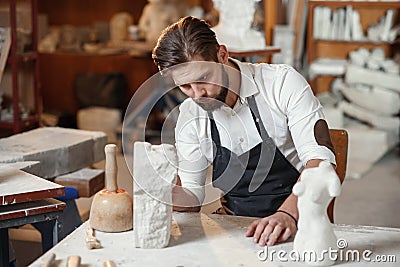 Bearded sculptor measures stone woman torso to make copy of it from limestone at creative studio. Stock Photo