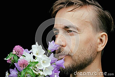 Handsome bearded stylish man sniffs aroma of tender wild flowers on black background. Gift for my love. Feeling nature Stock Photo