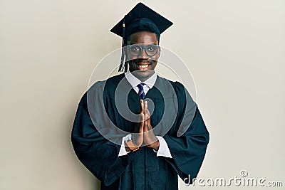 Handsome black man wearing graduation cap and ceremony robe praying with hands together asking for forgiveness smiling confident Stock Photo