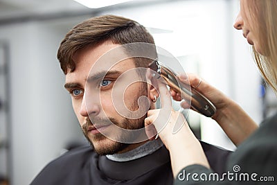 Handsome blue eyed man sitting in barber shop. Hairstylist Hairdresser Woman cutting his hair. Female barber Stock Photo