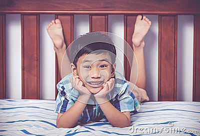 Handsome boy lying barefoot on bed in bedroom. Happy child smiling. Vintage tone effect. Stock Photo