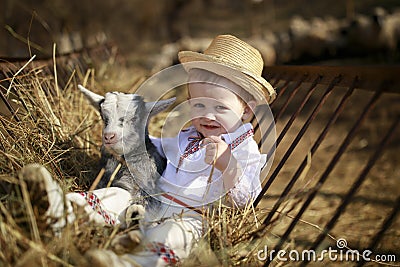 Handsome boy plays with the goatling in hay Stock Photo