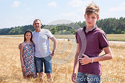 Handsome boy portrait with his father and preteen sister on background, Caucasian family in wheat field Stock Photo