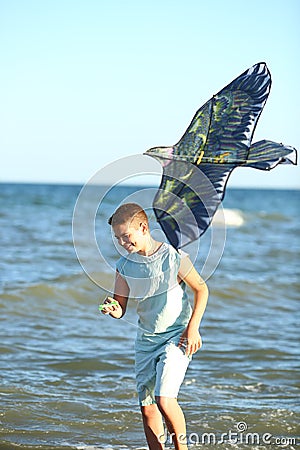 Handsome boy in shorts and a t-shirt teenager launches a kite on the sky on the seashore Stock Photo