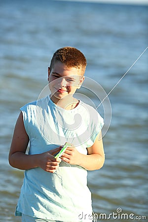 Handsome boy in shorts and a t-shirt teenager launches a kite on the sky on the seashore Stock Photo