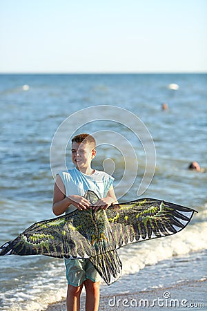 Handsome boy in shorts and a t-shirt teenager launches a kite on the sky on the seashore Stock Photo