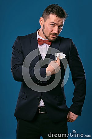 Man in black classic suit and red bow-tie showing two playing cards while posing against blue studio background Stock Photo