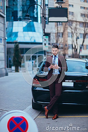 Handsome businessman entrepreneur standing proudly next to his parked limo at the middle of the business center Stock Photo
