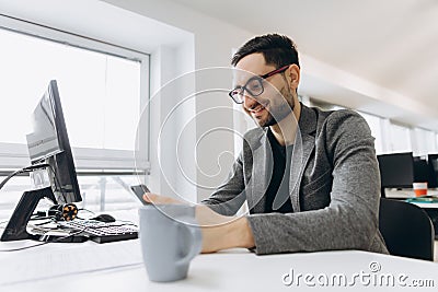 Handsome businessman is using a smartphone and smiling while working in office Stock Photo