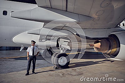 Handsome captain in hat looking into the distance in front of civil aircraft Stock Photo