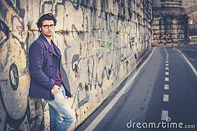 Handsome and charming young man outdoors leans against a wall in the city Stock Photo