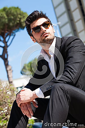 Handsome and charming young man with sunglasses sitting outdoors Stock Photo