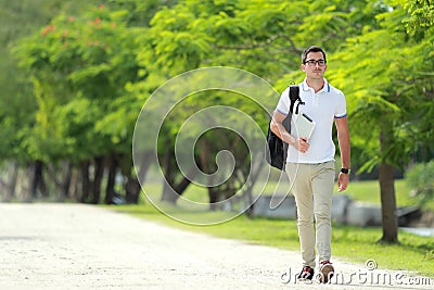 handsome college student walking by at college park with backpack and holding a tablet Stock Photo