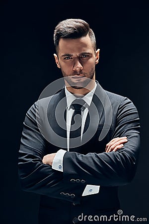Handsome confident man in black suit with arms crossed on dark background Stock Photo