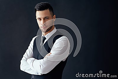 Handsome confident man in elegant suit with crossed arms on black background Stock Photo