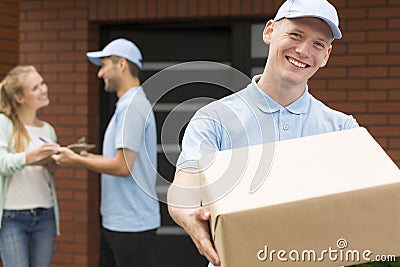 Courier in blue uniform holding big brown package and smiling Stock Photo