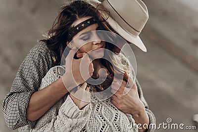 Handsome cowboy man in white hat touching cheek of beautiful boho gypsy woman with leather headband, face closeup portrait Stock Photo