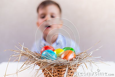 A boy looks with interest and curiosity at a basket with multi-colored Easter eggs on a table on a white background Stock Photo