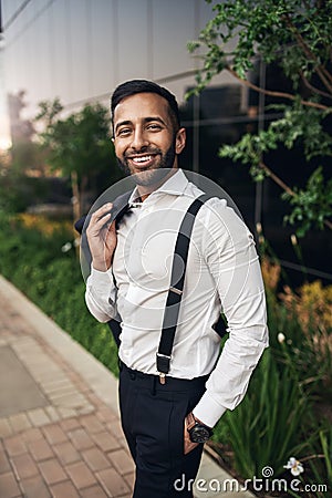 Handsome dapper bearded smiling Indian businessman standing with jacket over shoulder Stock Photo