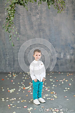 Handsome dark-haired boy in a white shirt, turquoise pants and white sneakers on a gray Stock Photo